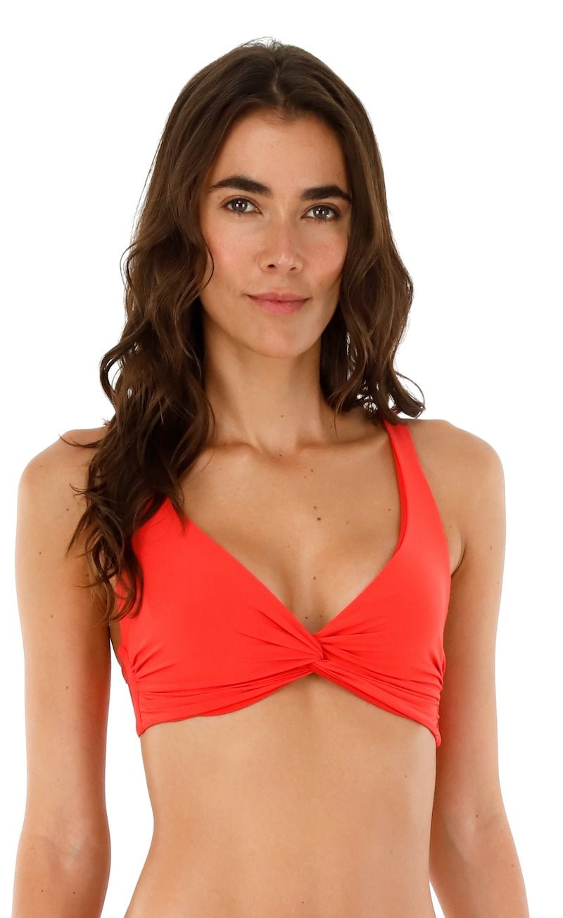 Image of a woman wearing a red swimsuit top by Malai Swimwear. She's smiling and standing on a white background. The purpose of this image is to highlight the bikini.
