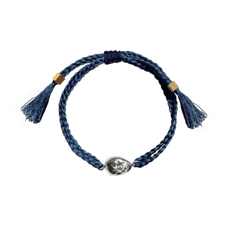 Image of an adjustable bracelet made of braided string and with a face charm on it. It's set against a white background. The purpose of this image is to highlight the jewelry by PAJAROLIMON.
