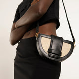 Person wearing a black outfit with a black and beige handbag on a plain background.