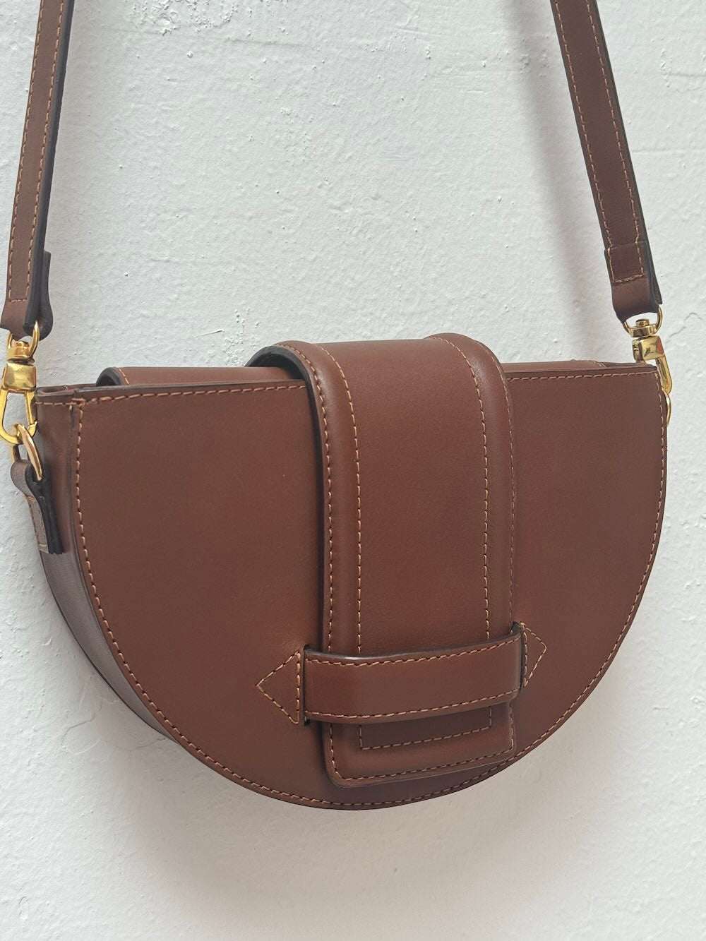 Brown leather handbag with gold hardware on a light gray background.