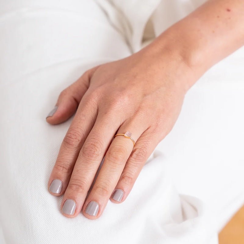 Close up image of a woman's hand wearing a dainty gold ring with a raw rose quartz stone on it. The purpose of this image is to highlight the ring because it is for sale at EVAMAIA boutique in Studio City, CA and online.