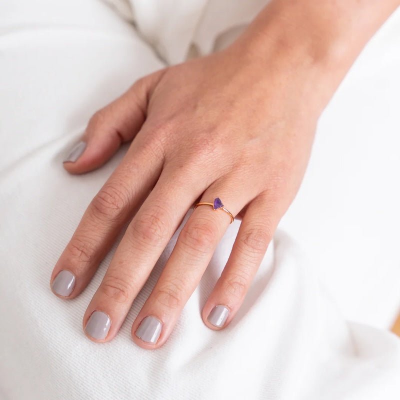 Close up image of a woman's hand wearing a dainty gold ring with a raw amethyst stone on it. The purpose of this image is to highlight the ring because it is for sale at EVAMAIA boutique in Studio City, CA and online.