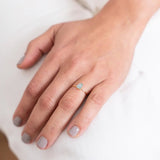 Close up image of a woman's hand wearing a dainty gold ring with a raw aquamarine stone on it. The purpose of this image is to highlight the ring because it is for sale at EVAMAIA boutique in Studio City, CA and online.