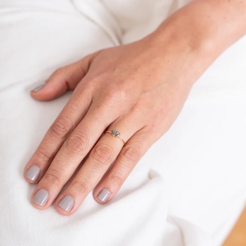 Close up image of a woman's hand wearing a dainty gold ring with a raw pyrite stone on it. The purpose of this image is to highlight the ring because it is for sale at EVAMAIA boutique in Studio City, CA and online.