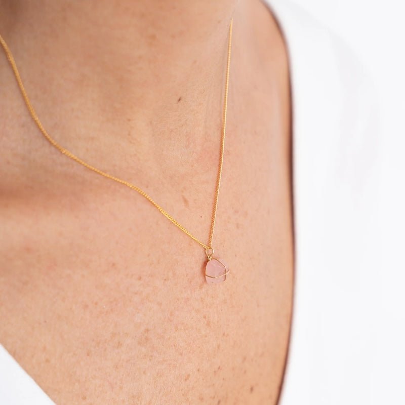 Close up image of a woman wearing a gold necklace with a rose quartz charm. The purpose of this image is to highlight the necklace by Wish Jewelry because it's sold at EVAMAIA boutique in Studio City, CA.