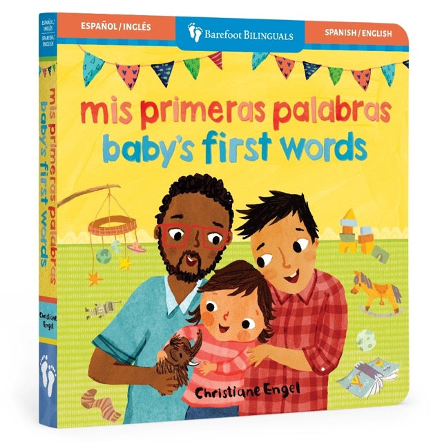 Board book cover of 'Mis primeras palabras - Baby's First Words' featuring illustrations of a family with two dads, a baby, and various colorful objects.