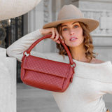 Woman holding a red handbag wearing a beige hat and white off-shoulder top with a blurred architectural background.