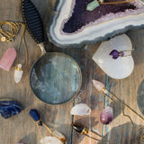 Image of perfume bottles made out of stone sitting on a raw amethyst stone. The purpose of this image is to highlight the perfume bottles, which can be worn as necklaces. They are made by Pajarolimon and sold at EVAMAIA boutique.