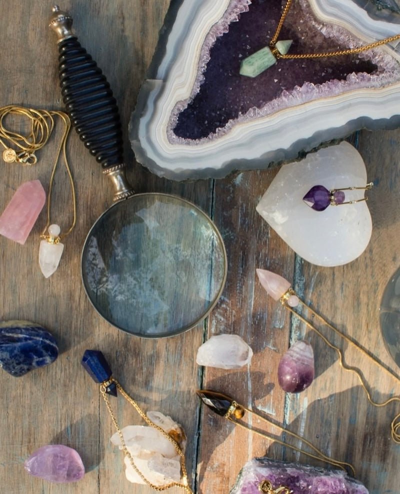 Image of perfume bottles made out of stone sitting on a raw amethyst stone. The purpose of this image is to highlight the perfume bottles, which can be worn as necklaces. They are made by Pajarolimon and sold at EVAMAIA boutique.