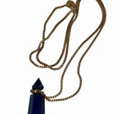 Image of a gold necklace holding a blue stone perfume bottle. The purpose of this image is to highlight the necklace. This necklace is made in Colombia by Pajarolimon and sold at EVAMAIA boutique.