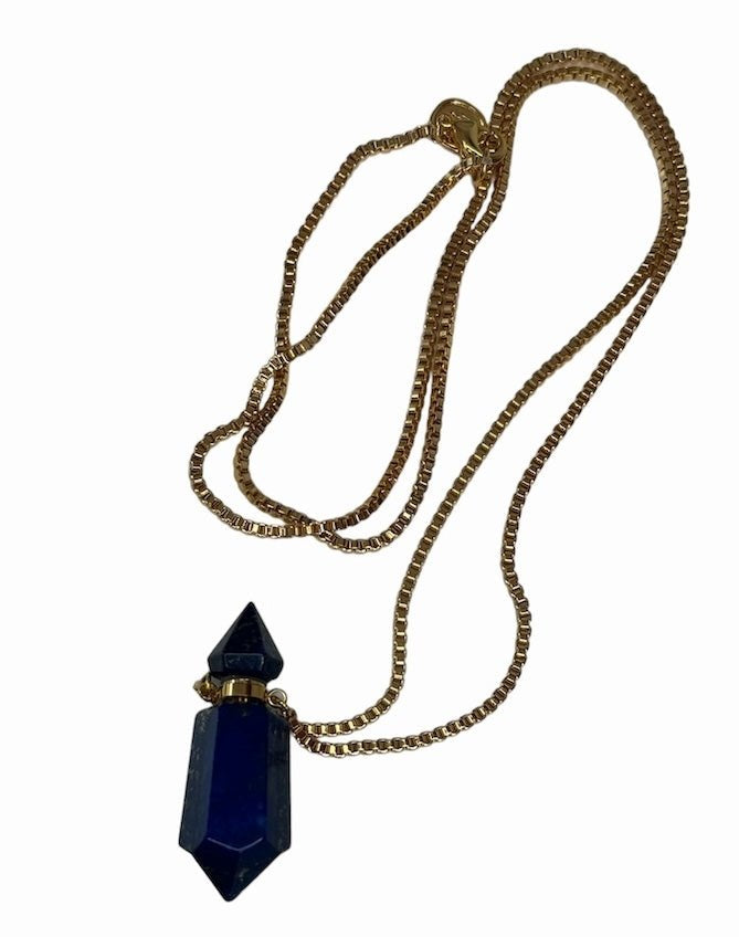 Image of a gold necklace holding a blue stone perfume bottle. The purpose of this image is to highlight the necklace. This necklace is made in Colombia by Pajarolimon and sold at EVAMAIA boutique.