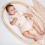 Baby lying in a wicker crib with a textured blanket.