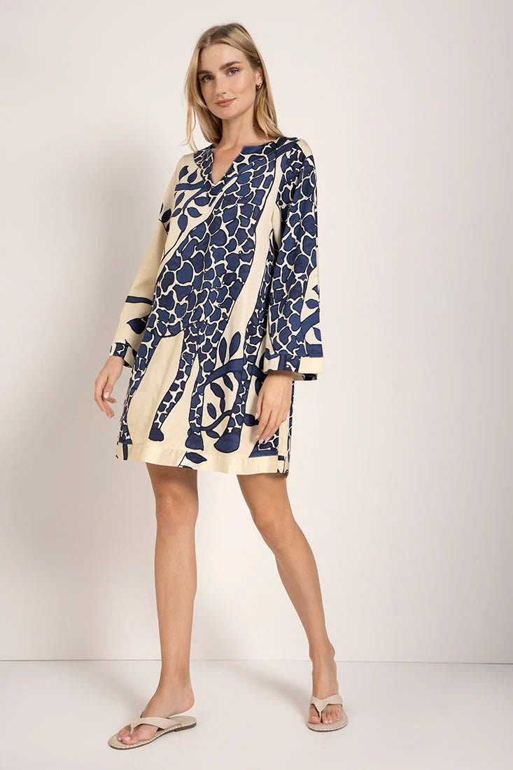 Model wearing a giraffe print cover-up dress with long sleeves. She's standing against a white background and looking at the camera. The purpose of this image is to highlight the dress.