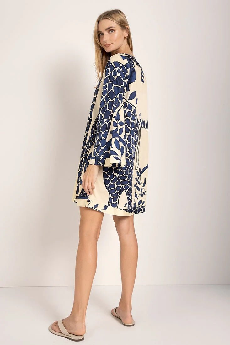Model wearing a giraffe print cover-up dress with long sleeves. She's standing against a white background and looking at the camera. The purpose of this image is to highlight the dress.