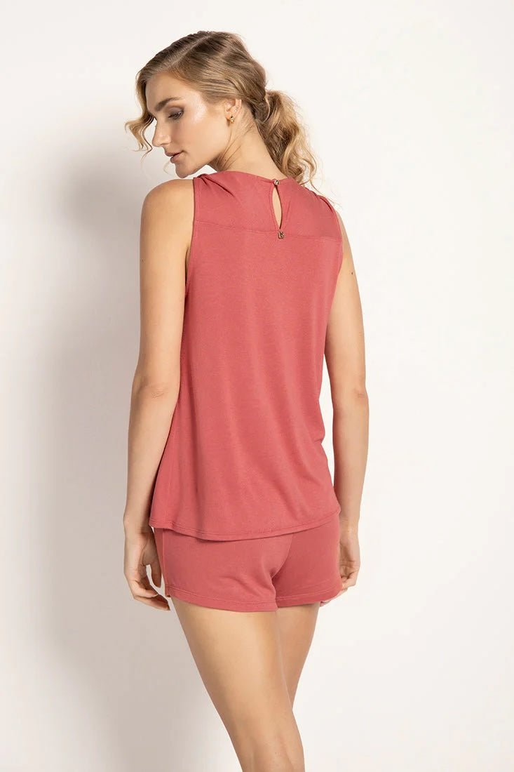 Model wearing a rose colored pajama set. The top is sleeveless. She's looking to the side and showing her back. She's in front of a white wall. The purpose of this image is to highlight the clothing.