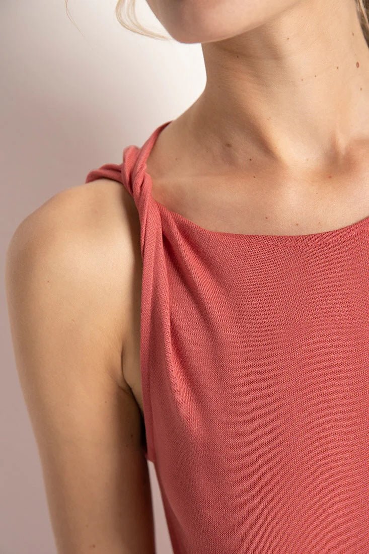 Close up image of a woman wearing a rose colored pajama set. The sleeves on the top look folded. She's standing in front of a white wall. The purpose of this image is to highlight the folded sleeve detail.