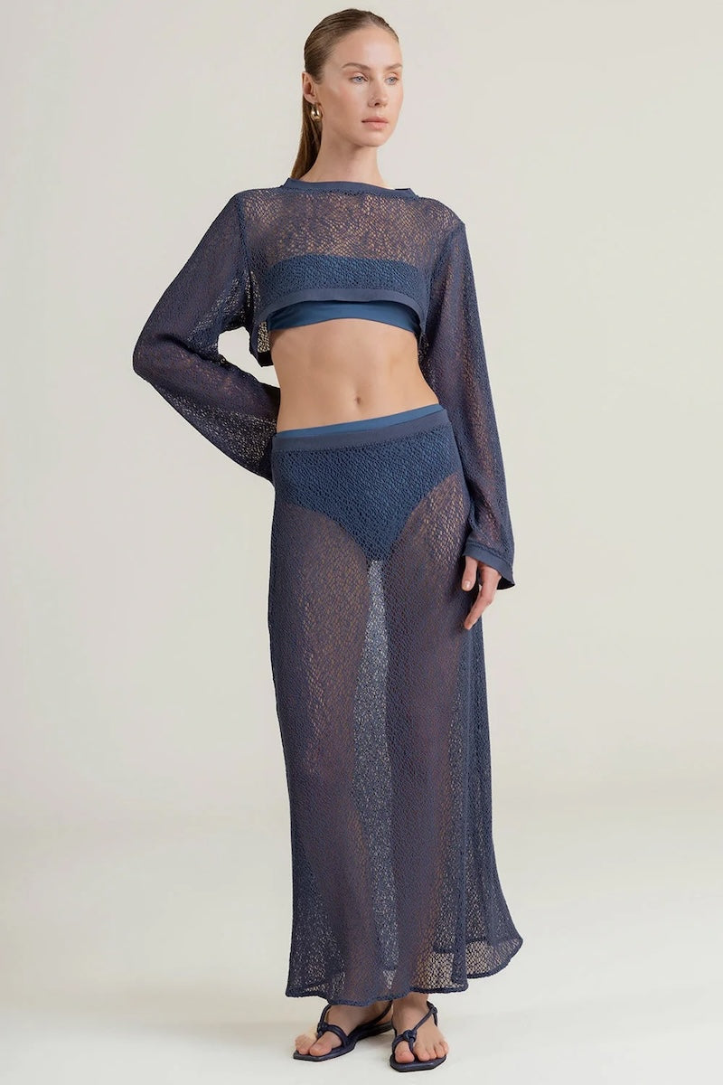 Woman wearing a dark blue sheer top with a matching maxi skirt on a light background.