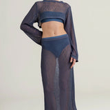 Woman wearing a dark blue sheer top with a matching maxi skirt on a light background.