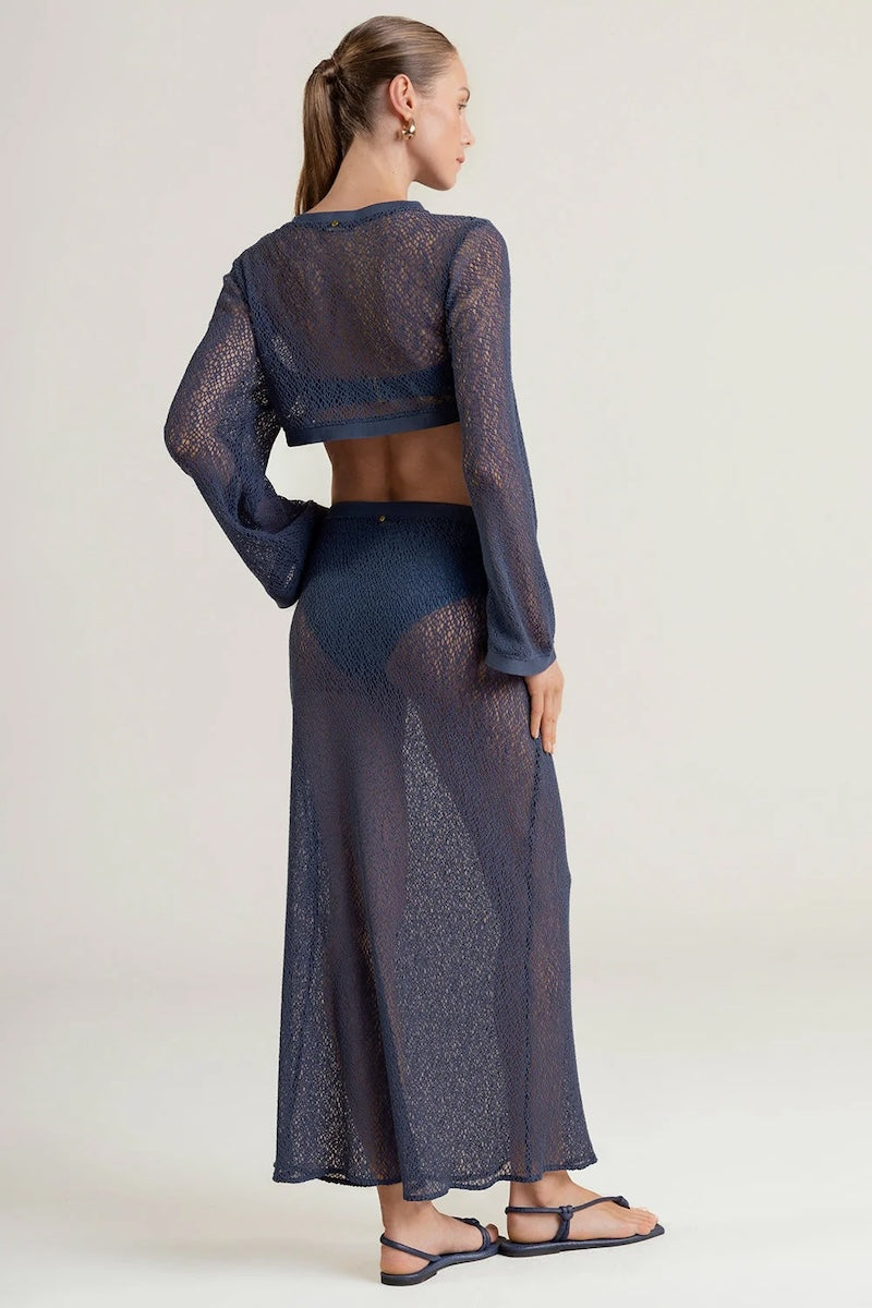 Woman wearing a mesh dark blue long sleeve with a matching maxi skirt on a plain background.