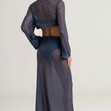 Woman wearing a mesh dark blue long sleeve with a matching maxi skirt on a plain background.