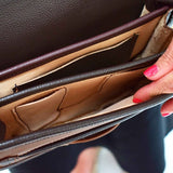 A two-toned brown leather crossbody saddle bag with multiple pockets and hardware accents, handmade in Colombia.