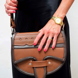 A two-toned brown leather crossbody saddle bag with multiple pockets and hardware accents, handmade in Colombia.