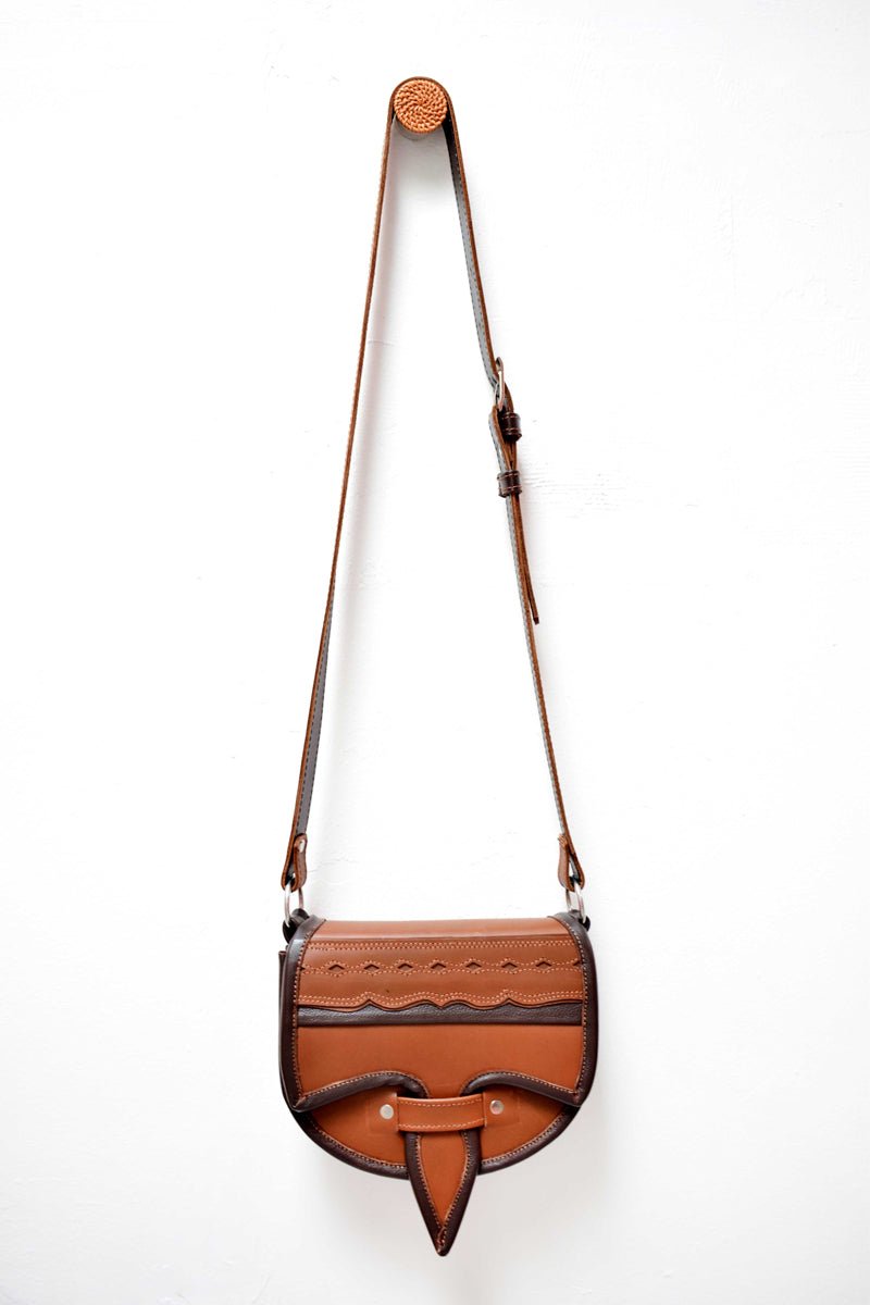 A two-toned brown leather crossbody saddle bag with multiple pockets and hardware accents, handmade in Colombia.