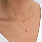 Close up image of a woman's neckline. She's wearing two necklaces. One has a charm of a Pisces zodiac sign and the other has a Fluorite stone. The purpose of this image is to highlight the necklaces, which are made in Colombia and sold in Studio City, at EVAMAIA boutique.