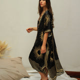 She is looking at us wearing the black golden suns kimono. She paired the kimono with brown open back slip ons. She is standing on a simple decor background.