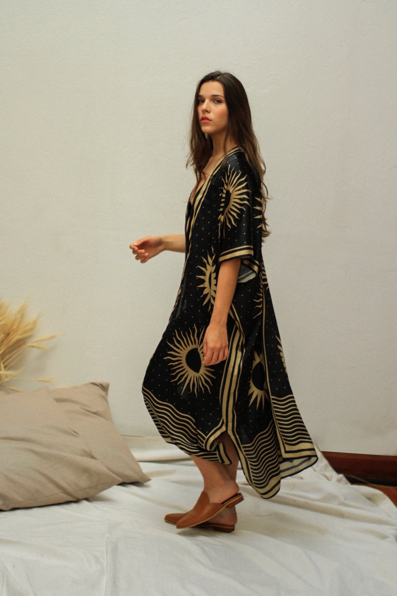 She is looking at us wearing the black golden suns kimono. She paired the kimono with brown open back slip ons. She is standing on a simple decor background.