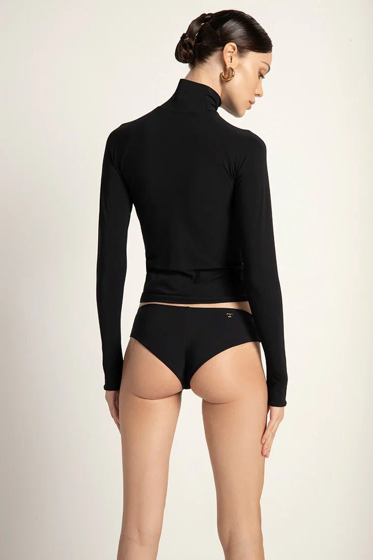 A female model wearing a black long-sleeved rashguard with thumb holes and a turtleneck, paired with black bikini bottoms.