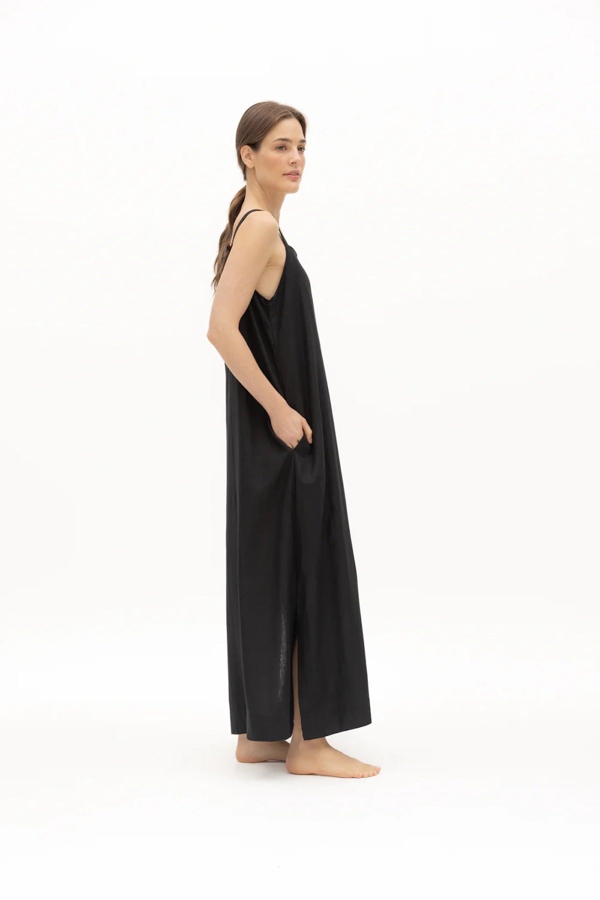 Image of a woman wearing a long dress with pockets and spaghetti straps that was made in Colombia by NAOS. The purpose of this image is to highlight the dress, which is for sale at EVAMAIA boutique in Studio City, CA and online.
