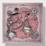 Zodiac Scarf for Libra made by Plissé. Image of scales. It is on top of a astrological background. Details like a white ecliptic, sun, and moon. The scarf is pink with white details displayed on plain background.