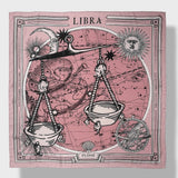 Zodiac Scarf for Libra made by Plissé. Image of scales. It is on top of a astrological background. Details like a white ecliptic, sun, and moon. The scarf is pink with white details displayed on plain background.