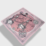 Zodiac Scarf for Libra made by Plissé. Image of scales. It is on top of a astrological background. Details like a white ecliptic, sun, and moon. The scarf is pink with white details floating on plain background.