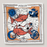 Zodiac Scarf for Pisces made by Plissé. Image of two fish swimming in opposite directions. It is on top of a astrological background. Details of a dark blue ecliptic, sun, moon, and a boat. The scarf is a white with orange and blue details displayed on top of a plain white background.