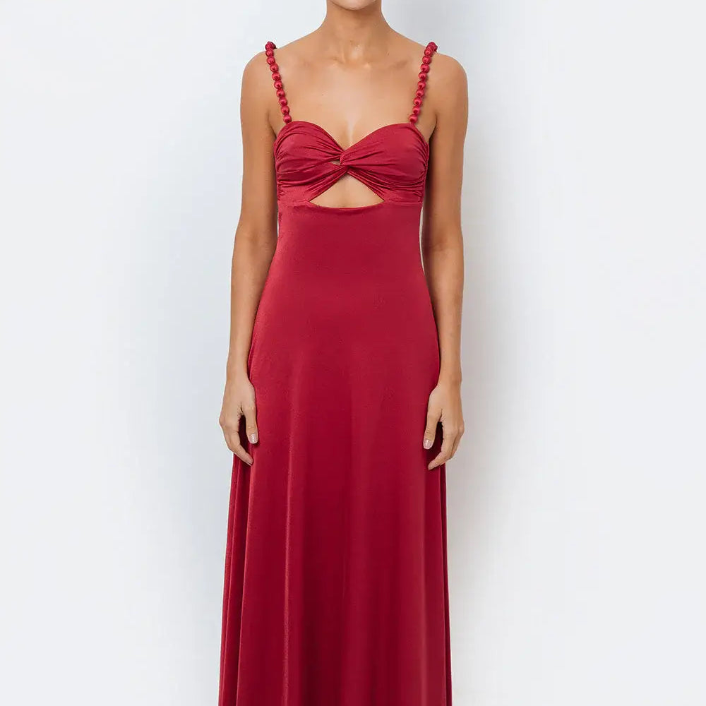 A woman modeling a deep crimson, flowy maxi dress with a sweetheart knotted bodice, center cutout, and pearl-accented straps.