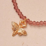 Necklace with a gold butterfly charm on a pink beaded chain against a beige background