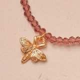 Necklace with a gold butterfly charm on a pink beaded chain against a beige background
