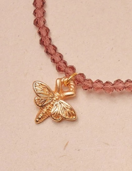 Necklace with a gold butterfly charm on a pink beaded chain against a beige background