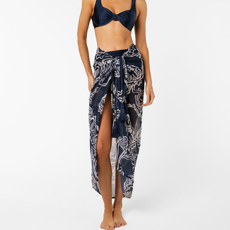 Woman wearing a navy bikini with a matching patterned sarong on a white background.