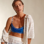 Woman wearing a blue bikini with a white crochet cover-up against a plain background. 