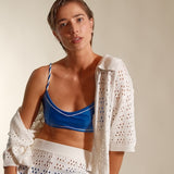 Woman wearing a blue bikini with a white crochet cover-up against a plain background. 
