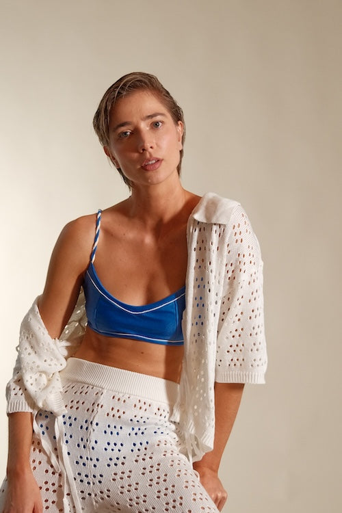 Woman wearing a blue bikini with a white crochet cover-up against a plain background. 