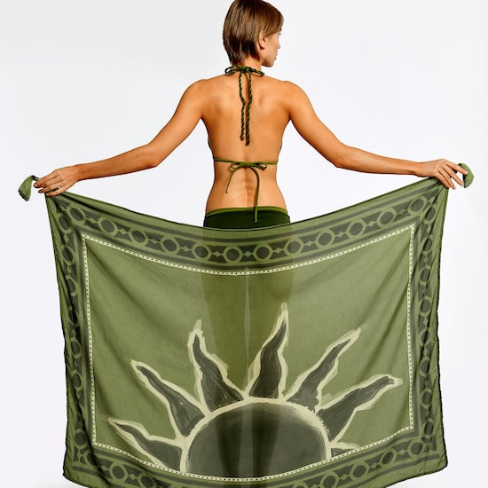 Woman holding a green sarong with a sun design on a white background. 