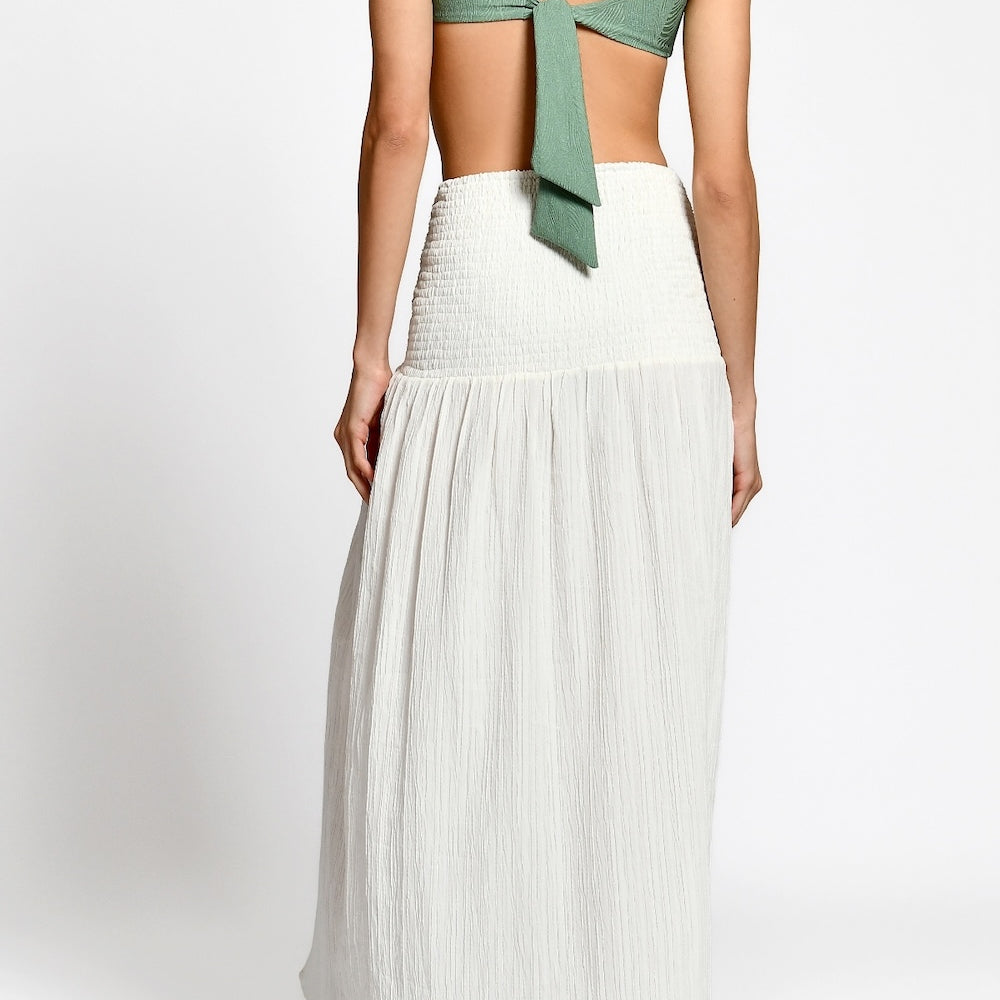 Woman wearing a green top and white pleated skirt on a white background.
