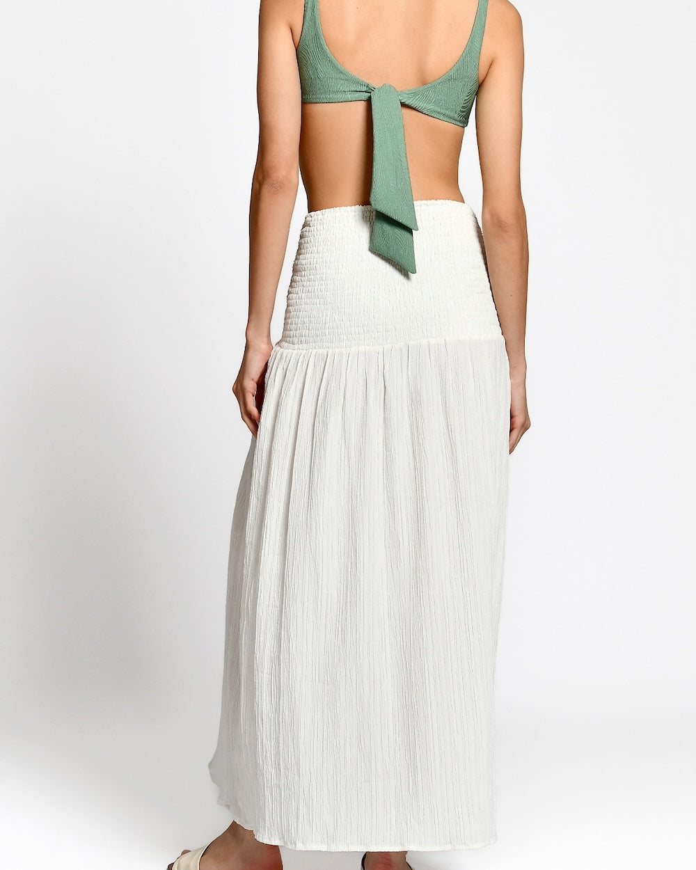 Woman wearing a green top and white pleated skirt on a white background.