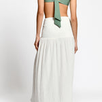 Woman wearing a green top and white pleated skirt on a white background.