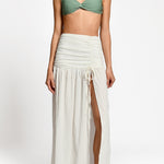 Woman wearing a green bikini top and white skirt on a white background