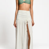 Woman wearing a green bikini top and white skirt on a white background